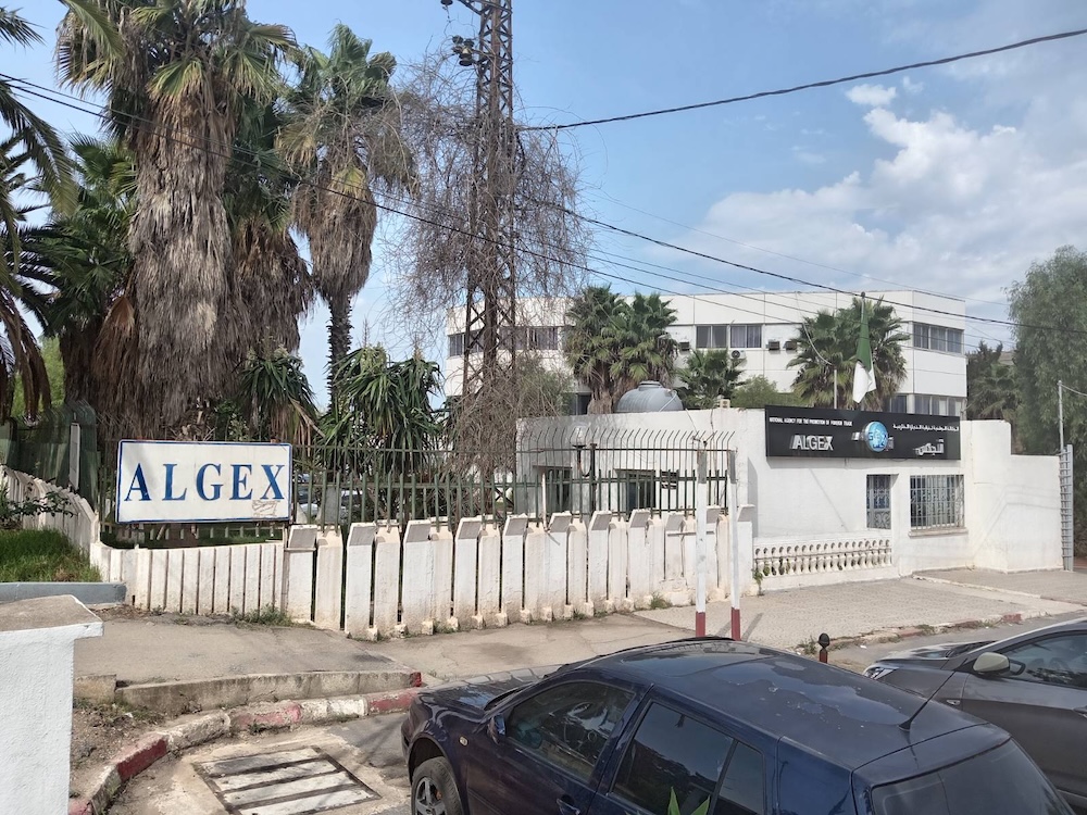 Vue extérieure du siège d’Algex à El Mohammadia, Alger, avec son panneau d’entrée et le bâtiment administratif derrière une clôture, photographié un jour ouvrable mais portes closes, illustrant le vide institutionnel qui suit la dissolution de l’agence.