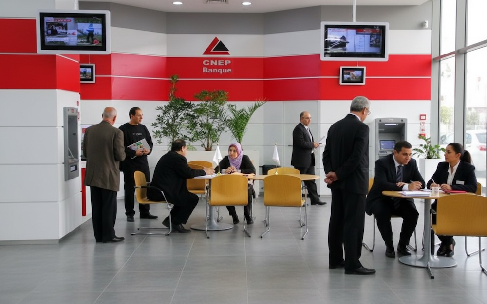 Intérieur d’une agence CNEP-Banque en Algérie, des clients assis aux guichets discutent avec des conseillers.