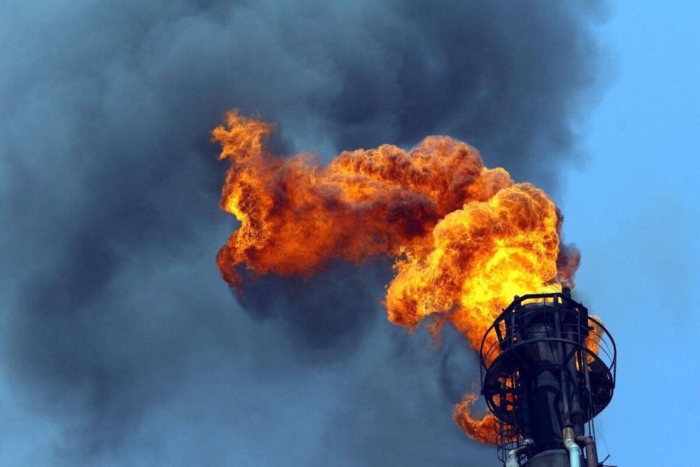 Torchère d'un site pétrolier produisant des flammes oranges et de la fumée noire sur fond de ciel bleu.