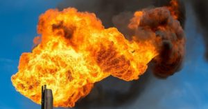 Flamme orange vif d'une torchère industrielle brûlant du gaz naturel sur fond de ciel bleu.