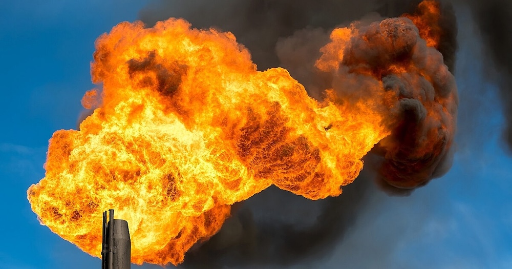 Flamme orange vif d'une torchère industrielle brûlant du gaz naturel sur fond de ciel bleu.