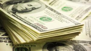 Liasses de billets de cent dollars américains empilés sur un fond de billets étalés.