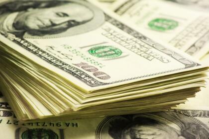 Liasses de billets de cent dollars américains empilés sur un fond de billets étalés.