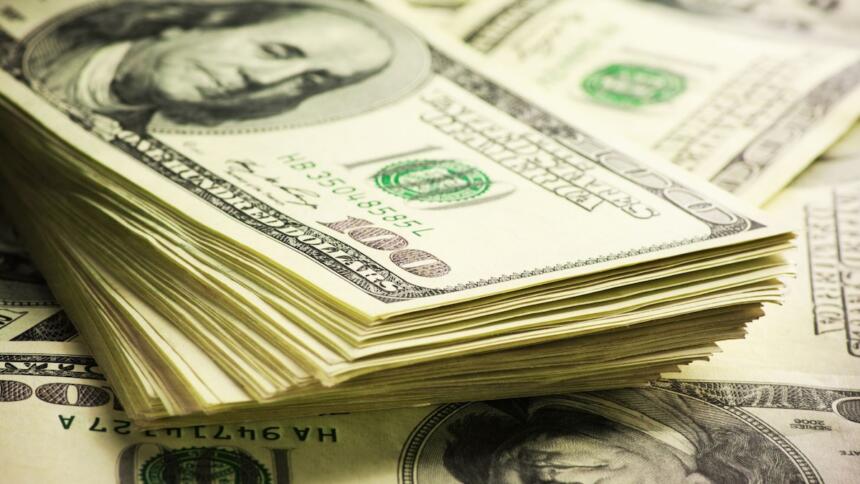 Liasses de billets de cent dollars américains empilés sur un fond de billets étalés.
