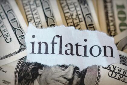 Mot inflation écrit sur un morceau de papier posé sur des billets de cent dollars américains