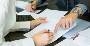 Deux personnes examinent un contrat de crédit posé sur un bureau, l'une pointe du doigt une clause du document pendant que l'autre s'apprête à signer avec un stylo.