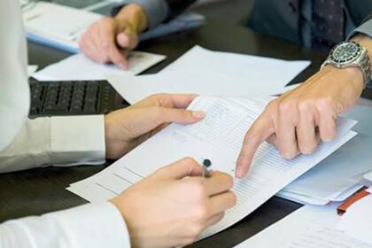 Deux personnes examinent un contrat de crédit posé sur un bureau, l'une pointe du doigt une clause du document pendant que l'autre s'apprête à signer avec un stylo.