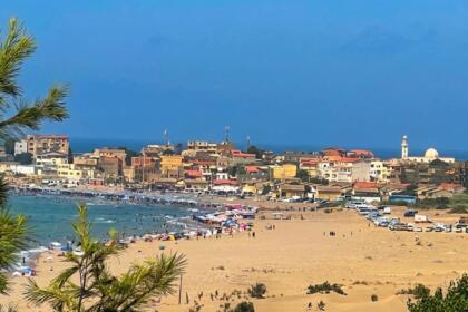 Vue depuis les dunes de Benyounes sur la plage de Zemmouri El Bahri, animée de baigneurs et de parasols, avec le village et le minaret de sa mosquée en arrière-plan, face à la Méditerranée