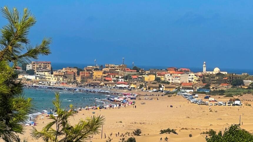 Vue depuis les dunes de Benyounes sur la plage de Zemmouri El Bahri, animée de baigneurs et de parasols, avec le village et le minaret de sa mosquée en arrière-plan, face à la Méditerranée