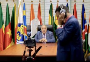 Farid Ghezali assis à un bureau devant le logo de l'APPO et les drapeaux de ses pays membres, filmé par une équipe de tournage lors d'une interview.