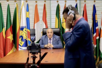 Farid Ghezali assis à un bureau devant le logo de l'APPO et les drapeaux de ses pays membres, filmé par une équipe de tournage lors d'une interview.