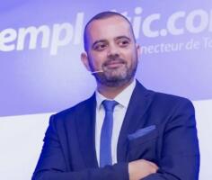Tarik Metnani, CEO d'Emploitic, bras croisés, micro-cravate, devant un fond floqué du logo Emploitic.com.