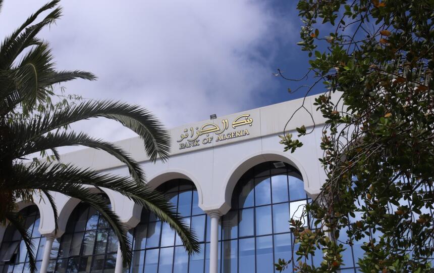 Façade du siège de la Banque d'Algérie à Alger, avec l'enseigne "Bank of Algeria" en arabe et en anglais, sous un ciel dégagé.