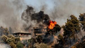 Immeuble d'habitation partiellement embrasé, entouré de fumée noire et de flammes, dans la végétation surplombant Souk El Tenine (Béjaïa).