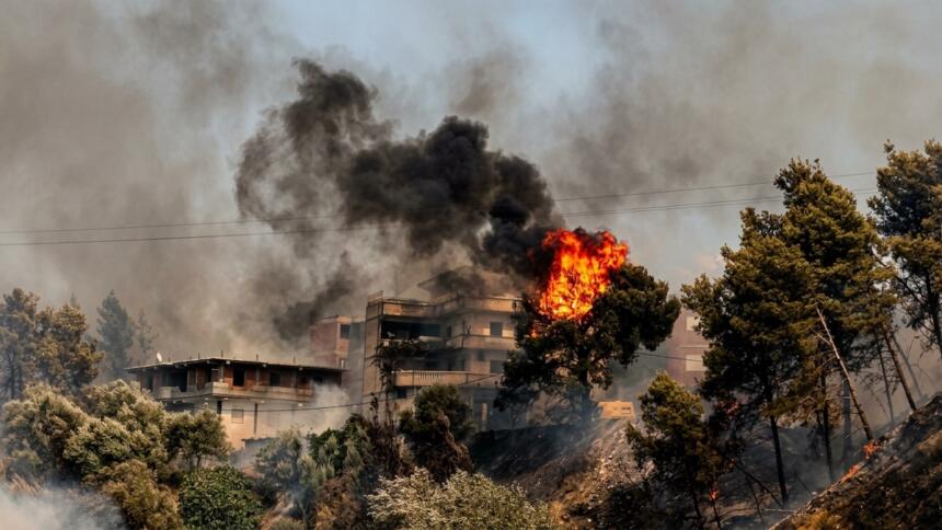 Immeuble d'habitation partiellement embrasé, entouré de fumée noire et de flammes, dans la végétation surplombant Souk El Tenine (Béjaïa).
