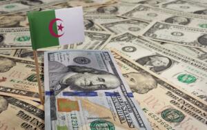 Drapeau algérien planté dans des billets de dollars américains, illustrant l'exposition de l'Algérie à la devise américaine.