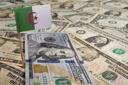 Drapeau algérien planté dans des billets de dollars américains, illustrant l'exposition de l'Algérie à la devise américaine.