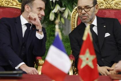 Emmanuel Macron et le roi Mohammed VI assis côte à côte, drapeaux français et marocain au premier plan.