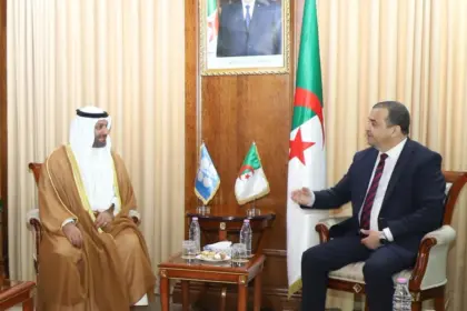 Mohamed Arkab, assis à droite, s'entretient avec Haitham Al-Ghais, en tenue traditionnelle du Golfe, dans un salon lambrissé du ministère des Hydrocarbures ; quatre responsables algériens en costume sont assis à gauche, sous le portrait du président et le drapeau algérien.