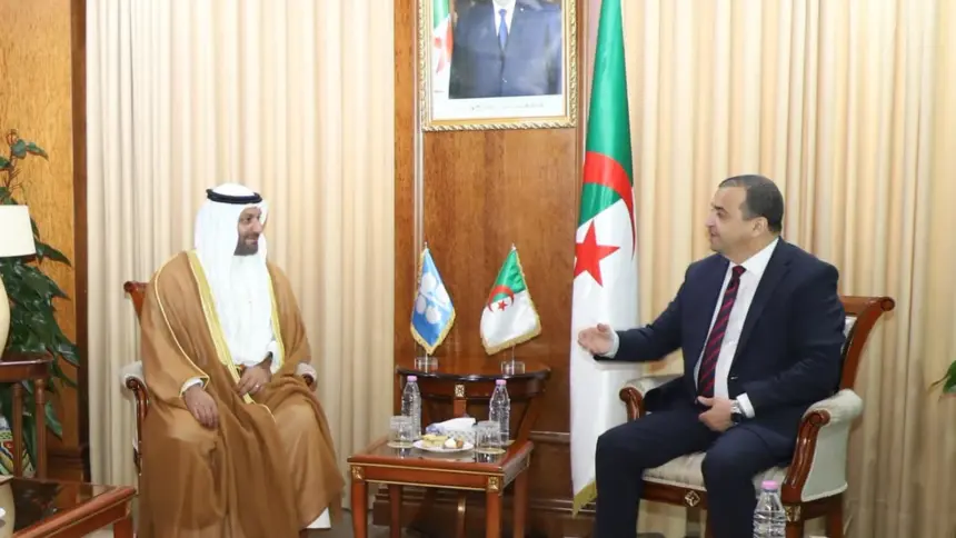 Mohamed Arkab, assis à droite, s'entretient avec Haitham Al-Ghais, en tenue traditionnelle du Golfe, dans un salon lambrissé du ministère des Hydrocarbures ; quatre responsables algériens en costume sont assis à gauche, sous le portrait du président et le drapeau algérien.