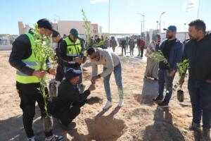 Groupe de bénévoles plantant de jeunes arbres sur un terrain sablonneux, certains en gilet fluorescent, sous un ciel dégagé.