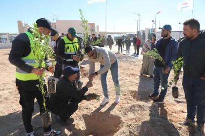 Groupe de bénévoles plantant de jeunes arbres sur un terrain sablonneux, certains en gilet fluorescent, sous un ciel dégagé.