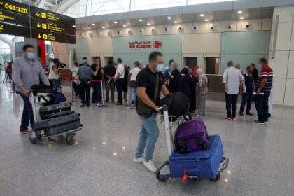 Passagers avec des chariots à bagages devant les comptoirs d’Air Algérie, illustrant la diaspora algérienne concernée par les transferts de fonds vers le pays.