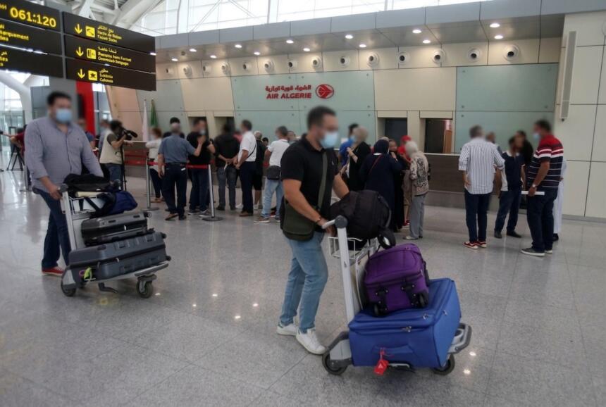 Passagers avec des chariots à bagages devant les comptoirs d’Air Algérie, illustrant la diaspora algérienne concernée par les transferts de fonds vers le pays.