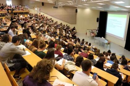 Amphithéâtre universitaire bondé, avec des étudiants assis sur des rangées de bancs en bois pendant un cours.