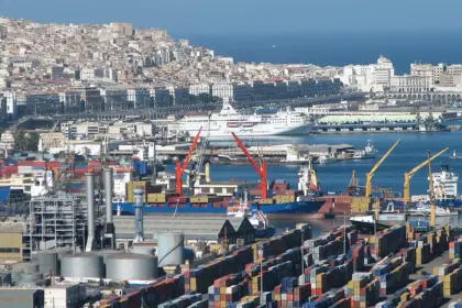 Vue du port d'Alger avec des conteneurs empilés, des grues de déchargement, un cargo à quai et la ville en arrière-plan