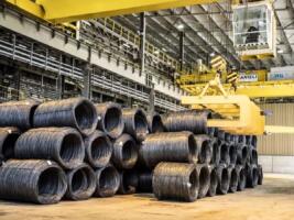 Bobines de fil machine en acier empilées dans une usine sidérurgique, avec un pont roulant industriel en arrière-plan.
