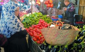 Étal de tomates, poivrons verts et aubergines sur un marché algérien, une cliente en hijab devant les cageots