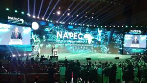 Mohamed Arkab au pupitre sur la scène du NAPEC 2025, devant un écran géant portant le logo du salon, face à une salle comble au Centre des conventions d’Oran.