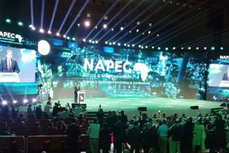 Mohamed Arkab au pupitre sur la scène du NAPEC 2025, devant un écran géant portant le logo du salon, face à une salle comble au Centre des conventions d’Oran.