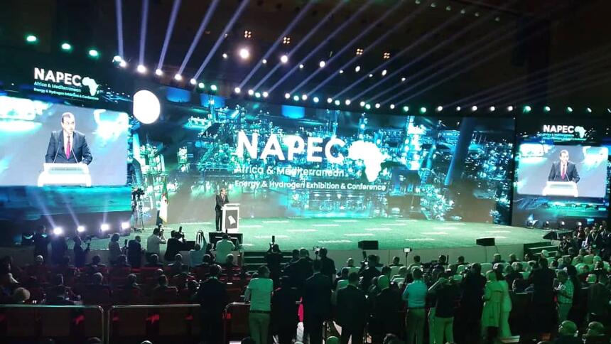 Mohamed Arkab au pupitre sur la scène du NAPEC 2025, devant un écran géant portant le logo du salon, face à une salle comble au Centre des conventions d’Oran.