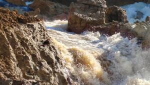 Torrent d'eau boueuse s'écoulant avec force entre des blocs de terre et de roche après la rupture de la conduite d'adduction Taksebt-Alger à Boudouaou