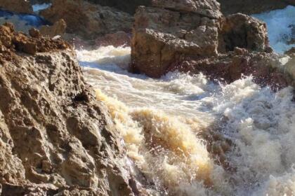 Torrent d'eau boueuse s'écoulant avec force entre des blocs de terre et de roche après la rupture de la conduite d'adduction Taksebt-Alger à Boudouaou