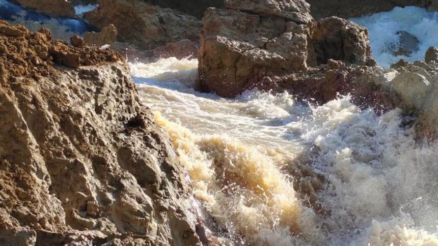 Torrent d'eau boueuse s'écoulant avec force entre des blocs de terre et de roche après la rupture de la conduite d'adduction Taksebt-Alger à Boudouaou
