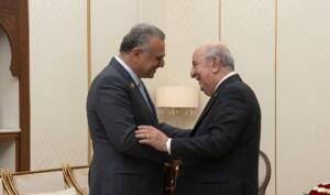 عبد المجيد تبون ومسعد بولس يتصافحان ويتبادلان الابتسام في صالون رئاسي بألوان كريمية وذهبية، بالجزائر العاصمة.