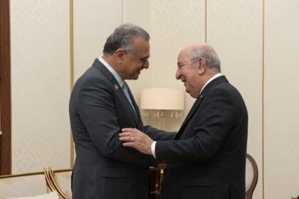 عبد المجيد تبون ومسعد بولس يتصافحان ويتبادلان الابتسام في صالون رئاسي بألوان كريمية وذهبية، بالجزائر العاصمة.