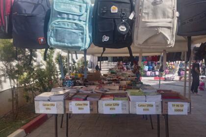 Étal de fournitures scolaires à Fréha avec cartables suspendus et cahiers étiquetés par prix (30 à 100 DA)