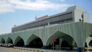 Façade verte à rayures et à grandes arcades du terminal de l’aéroport de Tripoli, avec des véhicules garés devant.