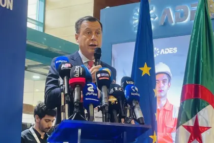 Un homme en costume sombre s'exprime au micro derrière un pupitre aux couleurs de l'Union européenne, entouré de micros de médias, devant les drapeaux européens et algériens.