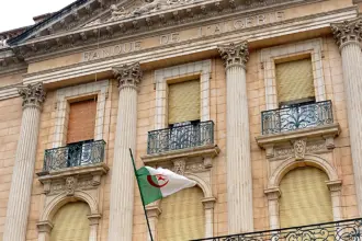 Façade néoclassique de la Banque d’Algérie, avec l’inscription « Banque de l’Algérie » et un drapeau algérien devant les colonnes.
