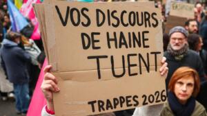 Une main tient une pancarte en carton où l’on lit en lettres noires « Vos discours de haine tuent – Trappes 2026 », devant des manifestants et des drapeaux colorés.