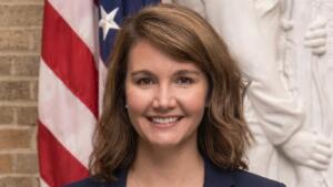 Rhiannon Elms, attachée agricole de l’ambassade des États-Unis, sourit en blazer bleu marine devant un drapeau américain