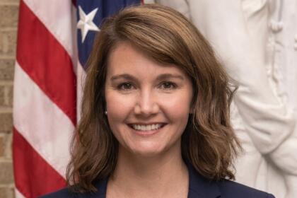 Rhiannon Elms, attachée agricole de l’ambassade des États-Unis, sourit en blazer bleu marine devant un drapeau américain
