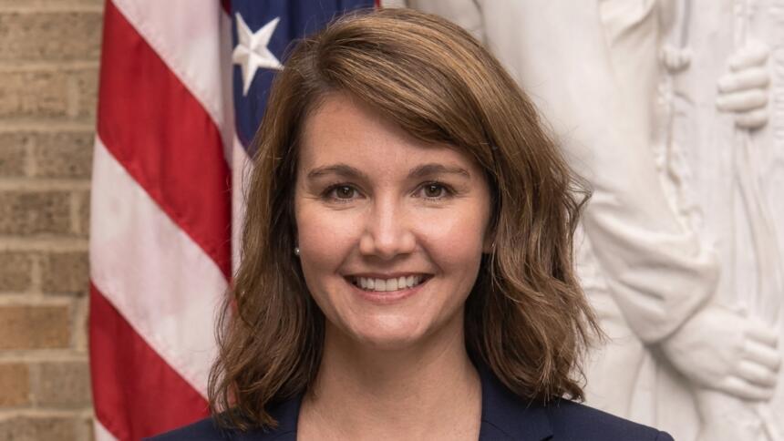 Rhiannon Elms, attachée agricole de l’ambassade des États-Unis, sourit en blazer bleu marine devant un drapeau américain