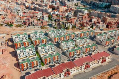 Vue aérienne d’un lotissement de villas jumelées aux toits verts et rouges, à Ali Mendjeli (Constantine), entouré de routes et de terrains en travaux.