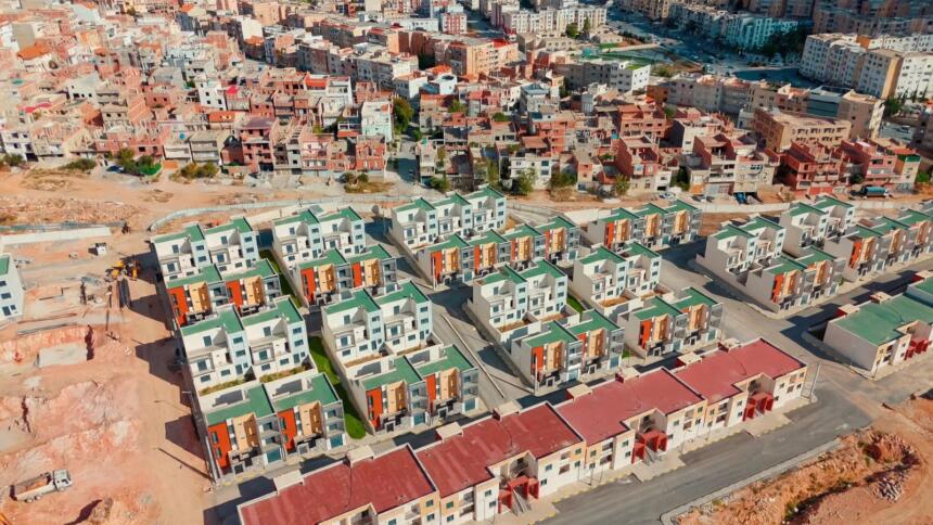 Vue aérienne d’un lotissement de villas jumelées aux toits verts et rouges, à Ali Mendjeli (Constantine), entouré de routes et de terrains en travaux.